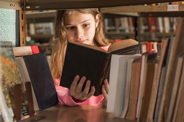 Free photo girl reading book behind bookshelf