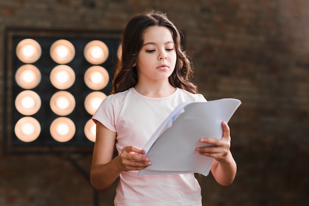 Free photo girl reading script standing against stage light