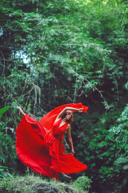 Free photo girl in a red dress dancing in a waterfall.