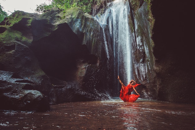 Free photo girl in a red dress dancing in a waterfall.