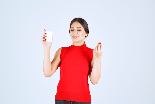 Girl in red shirt having coffee and showing positive sign.