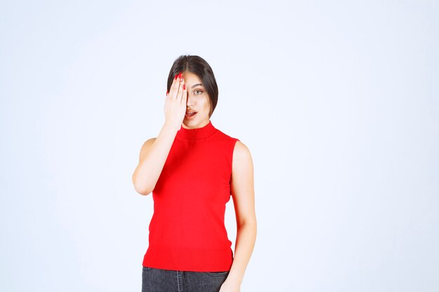 Girl in red shirt looking through her fingers.