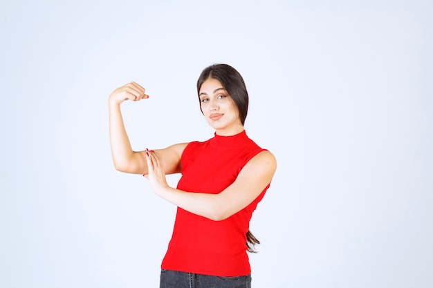 Girl in red shirt showing her arm muscles and fists.