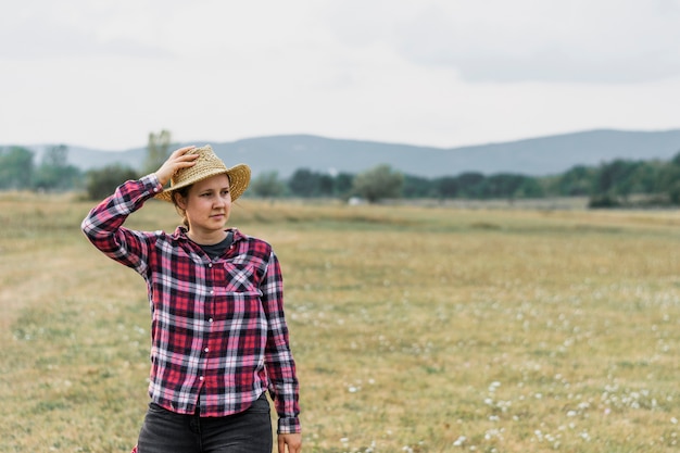 Girl in a red squared shit holding her hat in the field