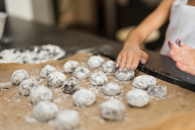 Free photo girl's hand applying flour on raw cookies