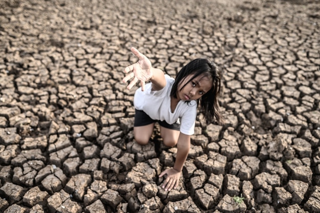 Free photo the girl sat elsewhere, hand to the sky to ask for rain on the dry ground, global warming