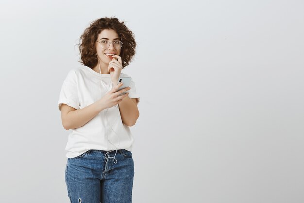 Girl sending risky text, looking excited, smiling and biting finger, holding mobile phone