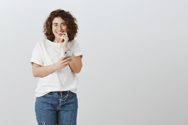 Girl sending risky text, looking excited, smiling and biting finger, holding mobile phone