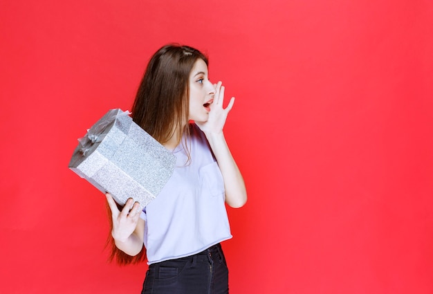 Girl shouting and calling someone to receive the silver gift box. 