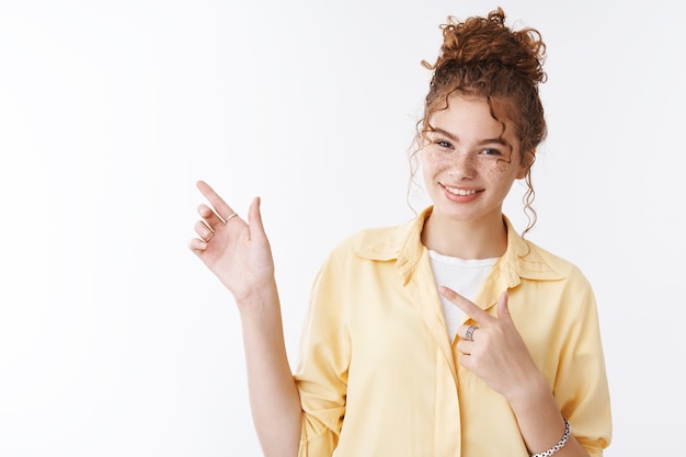 Girl showing direction pointing left smiling broadly give advice where go. Charming redhead cutie freckled cheeks grinning indicating place advertisement copy space, standing white background