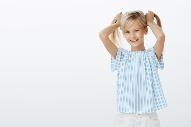 Girl showing friends her new earrings. Joyful pleased little girl with blond hair, lifting hair up and smiling joyfully