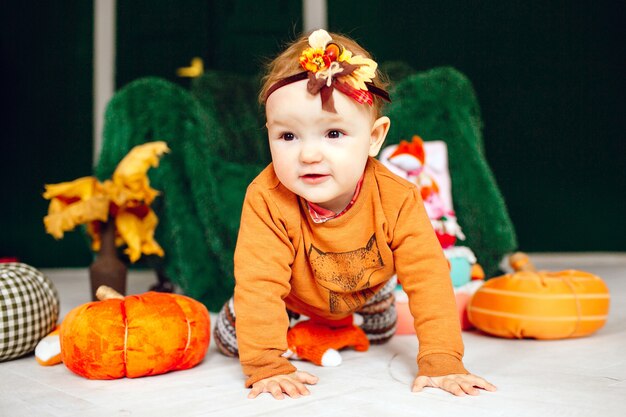 Girl sits among toy pumpkins before large green armchair 