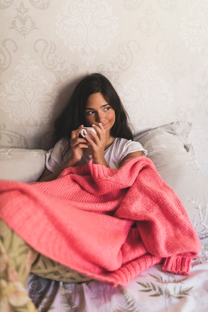 Free photo girl sitting on bed holding coffee cup looking away