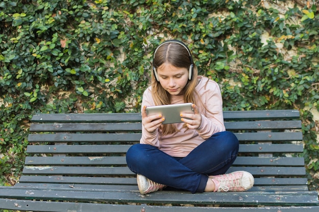 Girl sitting on bench wearing headphone using mobile phone in park