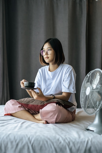 A girl sitting and drinking coffee on the bedroom.