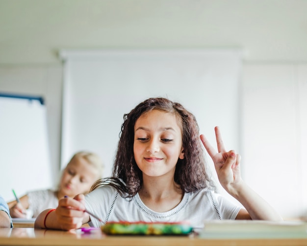 Girl sitting at school desk gesturing