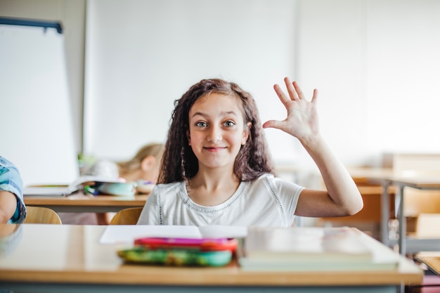 Girl sitting at school desk waving hand