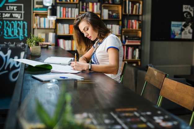 Free Photo girl sitting at table with notebooks writing