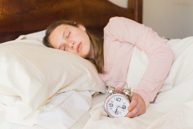 Girl sleeping with alarm clock on bed