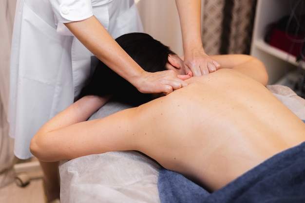 The girl in the spa salon receives a back and neck massage, lies in the cosmetology table, relaxed and enjoys the process