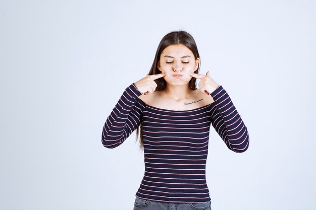 Girl in srtiped shirt looks ill and showing her mouth. 