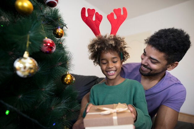 Girl standing by Christmas tree and unwrapping present box looking surprised