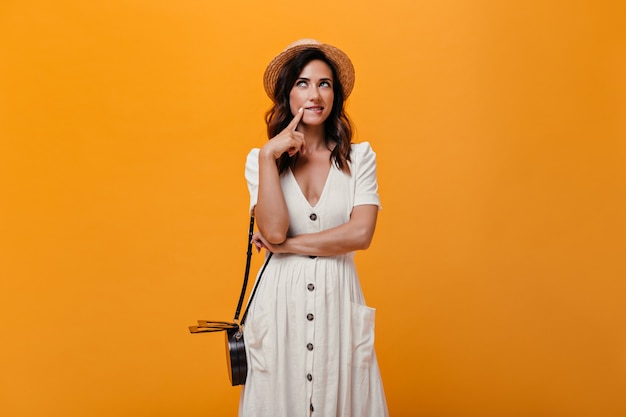 Girl in straw hat posing thoughtfully against orange background