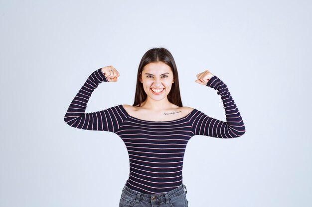 Girl in striped shirt demonstrating her arm muscles. 