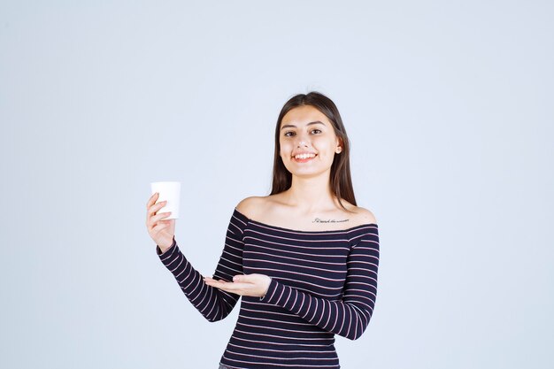 Girl in striped shirt holding a plastic coffee cup and looks positive.