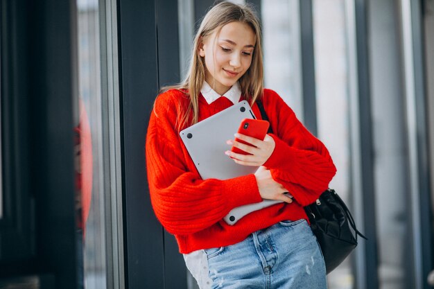 Girl student holding computer and talking on the phone by the window