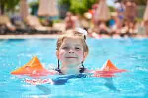 Free photo girl swimming in the pool in armlets on a hot summer day. family vacation in a tropical resort