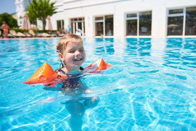 Girl swimming in the pool in armlets on a hot summer day. Family vacation in a tropical resort