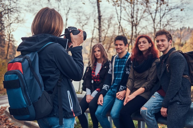 Free Photo girl taking a photo of her friends. group of young friends sitting on guardrail near road. travel, hiking, adventure concept.