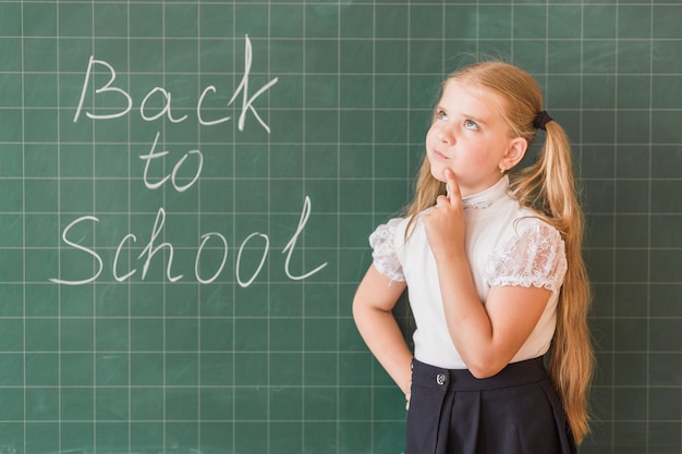 Girl thinking standing near blackboard