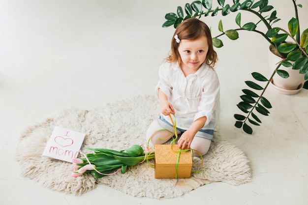 Free photo girl tying bow on gift box near greeting card