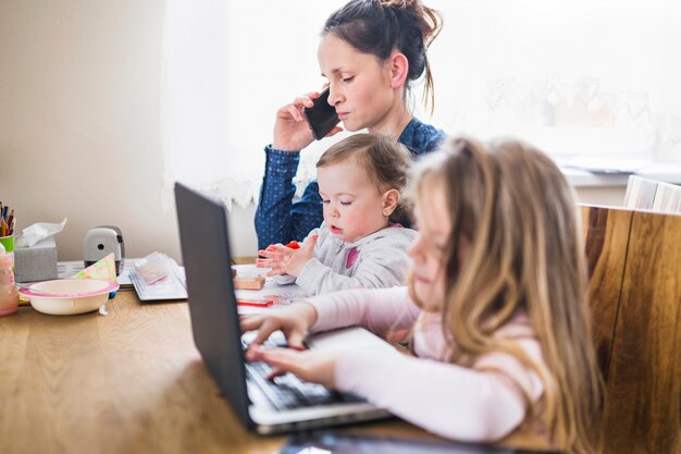 Girl using laptop beside her mother talking on smartphone