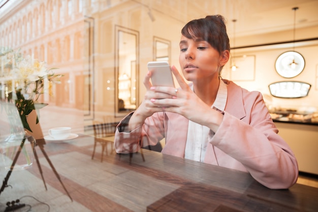 Free photo girl using mobile phone while sitting at the cafe table