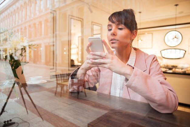 Girl using mobile phone while sitting at the cafe table