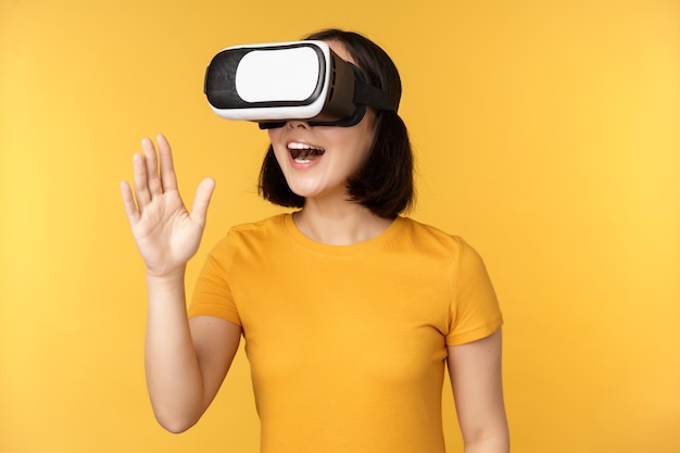 Girl in VR Beautiful young asian woman using virtual reality glasses and playing chatting virtually standing over yellow background