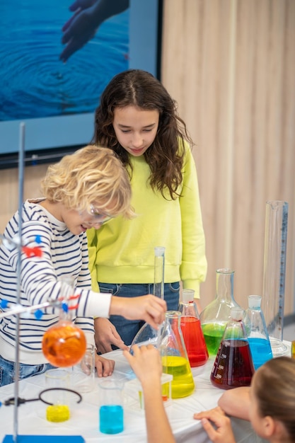 Girl watching boy lowering pipette into flask