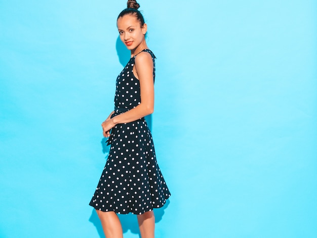 Free photo girl wearing polka-dot dress. model posing near blue wall in studio. positive female