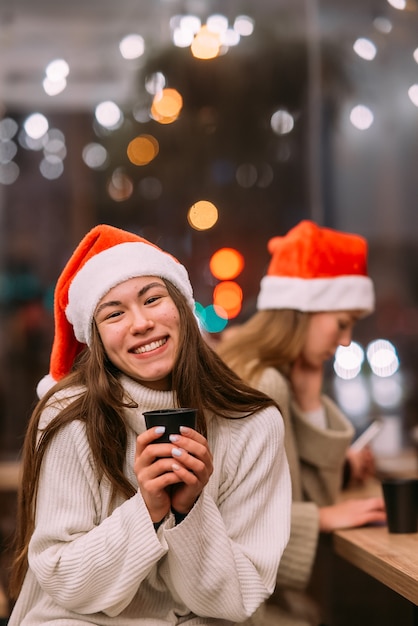 Girl wearing santa hat sitting in coffee shop and drinking coffee