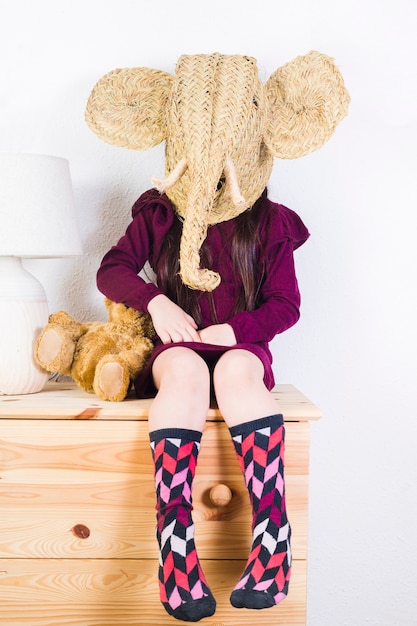 Free photo girl wearing wicker elephant mask sitting on table