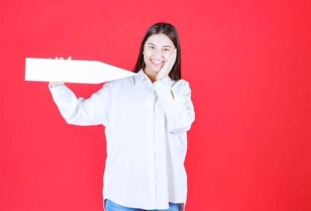 Girl in white shirt holding an arrow pointing to the right and looks confused or thoughtful