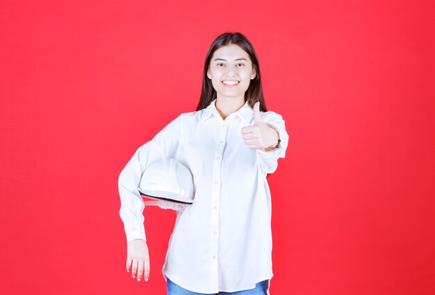 Girl in white shirt holding a white helmet and showing positive hand sign