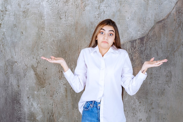 Free Photo girl in white shirt standing on a concrete wall and looks confused and thoughtful.