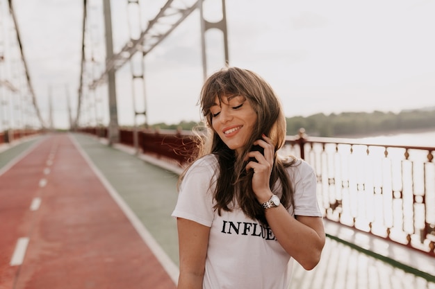 Free Photo girl in white t-shirt touching her hair and closing eyes while walking