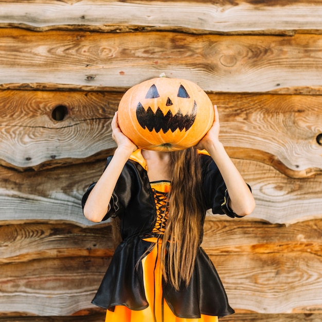 Free photo girl in witch costume closing face by pumpkin