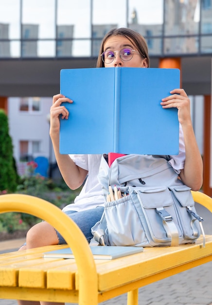 Free Photo a girl with a backpack near the school and a blue notebook on the background of the school