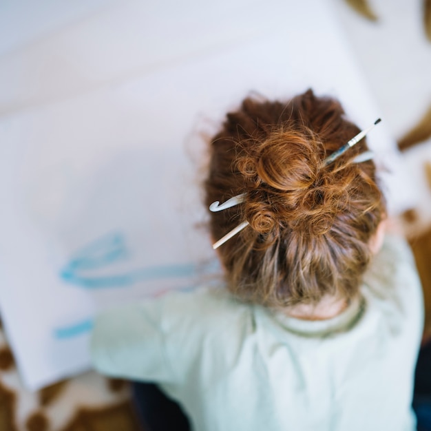 Free photo girl with brush in hairs painting on paper and sitting on floor